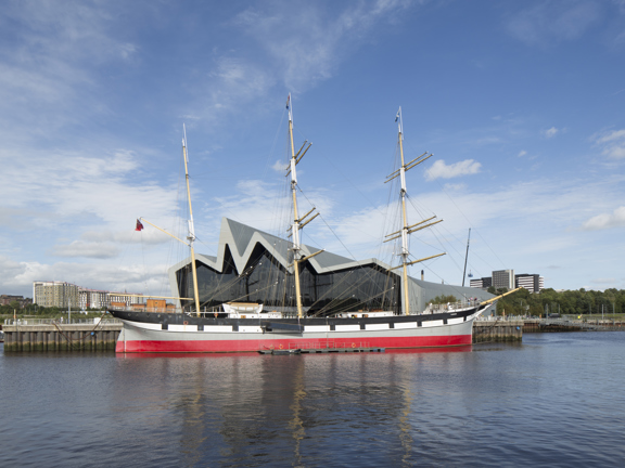 Sunny view of the modern, glass-fronted Riverside Museum, where the roofline reminiscent of a heartbeat on a monitor, with a three-masted 19th century Glenlee tallship docked outside.
